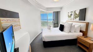 Una habitación de hotel moderna con una cama grande, una mesita de noche de madera, un televisor de pantalla plana y obras de arte en las paredes.