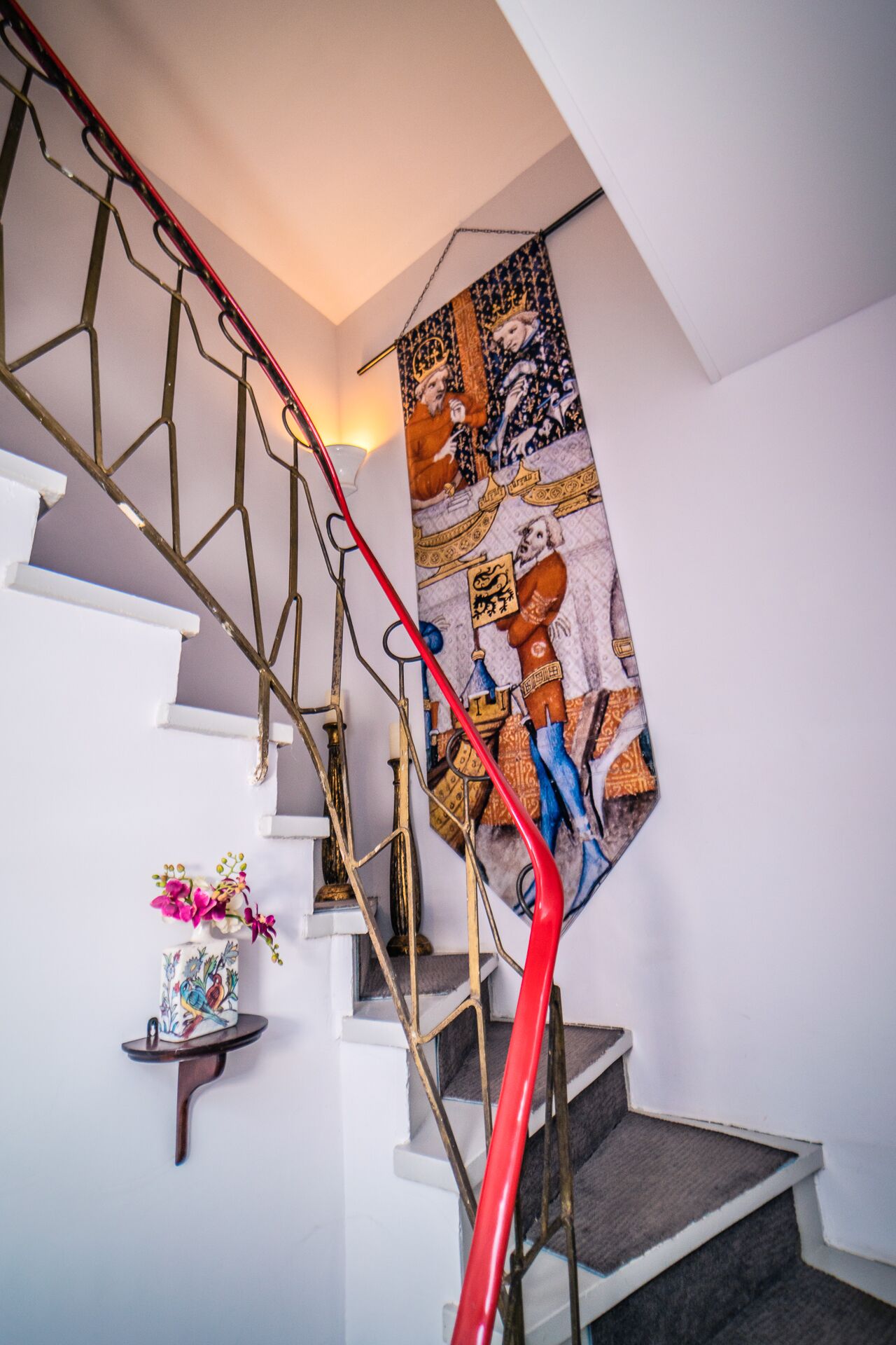 A staircase with a red handrail, white walls, and a decorative tapestry.