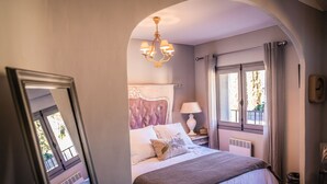 Une chambre à coucher avec un grand lit, un lustre, une fenêtre avec des rideaux et un radiateur.