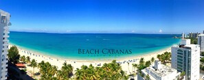 A beach view with a clear sky, palm trees, and a beach with umbrellas.
