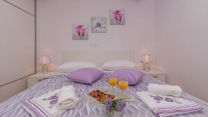A neatly made bed with pillows, a tray of croissants, two glasses of orange juice, and towels.