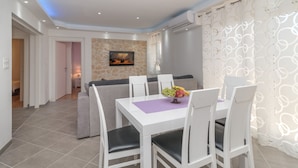 A dining area with a white table and chairs, a fruit bowl, and a stone wall with a painting.