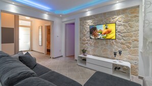 A modern living room with a stone accent wall, a flat-screen TV, a grey sofa, and a white entertainment unit.