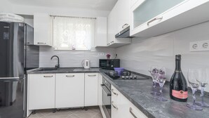 A modern kitchen with white cabinets, a stainless steel refrigerator, a microwave, and a gas stove. There are wine glasses and a bottle on the counter.