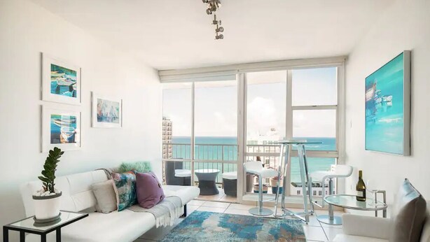 A spacious living room with a large balcony, white furniture, and artwork on the walls. - Ocean View  Studio  Apt In the heart of Condado 21 floor with parking  (San Juan)