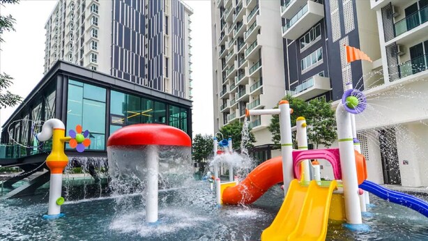 Un espace de jeux aquatiques en plein air, doté de toboggans et de jets d’eau, entouré de bâtiments modernes.