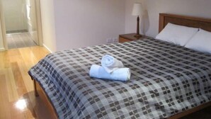 Een hotelkamer met een bed, een nachtkastje, een lamp en een deur naar een andere kamer.