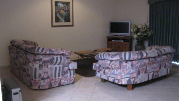 Ein Wohnzimmer mit zwei gemusterten Sofas, einem Fernseher auf einem Schrank und einem gerahmten Bild an der Wand.