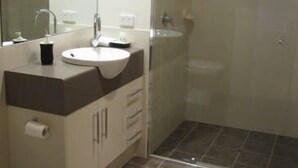Een badkamer met een wit wastafelmeubel, spiegel en toilet. Er is een douchecabine met een glazen deur.