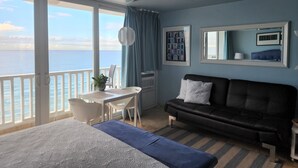 Une pièce comprenant un lit, un canapé en cuir noir, une table à manger avec des chaises, un ventilateur de plafond et une grande fenêtre donnant sur la mer.