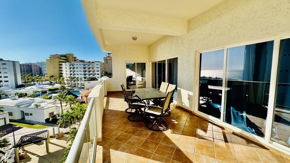 A balcony with a dining table and chairs, large windows, and a view of a cityscape and pool.