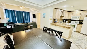 A modern kitchen with a dining area, featuring a large island, built-in appliances, and a view to the living area.