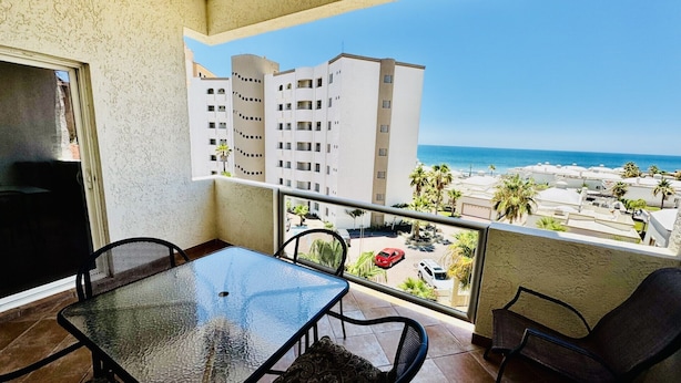 A balcony with a glass table and chairs, overlooking a beach and buildings. - Beautiful 2 Bedroom Condo on the Sea of Cortez at Las Palmas Resort D-404 (Puerto Peñasco)