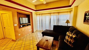 A living room with a sofa, a coffee table, a TV mounted on the wall, and a window with curtains. - Beautiful 2 Bedroom Condo on the Sea of Cortez at Las Palmas Resort D-404 (Puerto Peñasco)