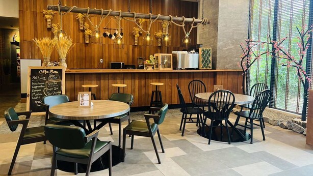 A cafe with wooden walls, a chalkboard menu, and a variety of seating options including round tables and chairs. - Super Hotel Thilawa (Yangon)