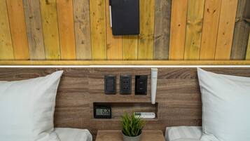 A wooden-paneled wall with a black notebook holder, three electrical outlets, a digital clock, and a potted plant.