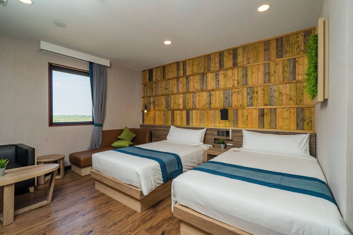 A hotel room with two beds, a small table, a TV, and a window with curtains.