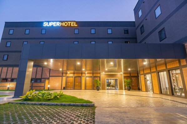 Una entrada de hotel moderna con un letrero de "SuperHotel", un área exterior cubierta y fachada de ladrillo.