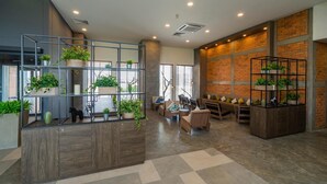 A modern interior with a wooden reception desk, metal shelving with plants, a seating area with sofas, and a brick wall. - Super Hotel Thilawa (Yangon)