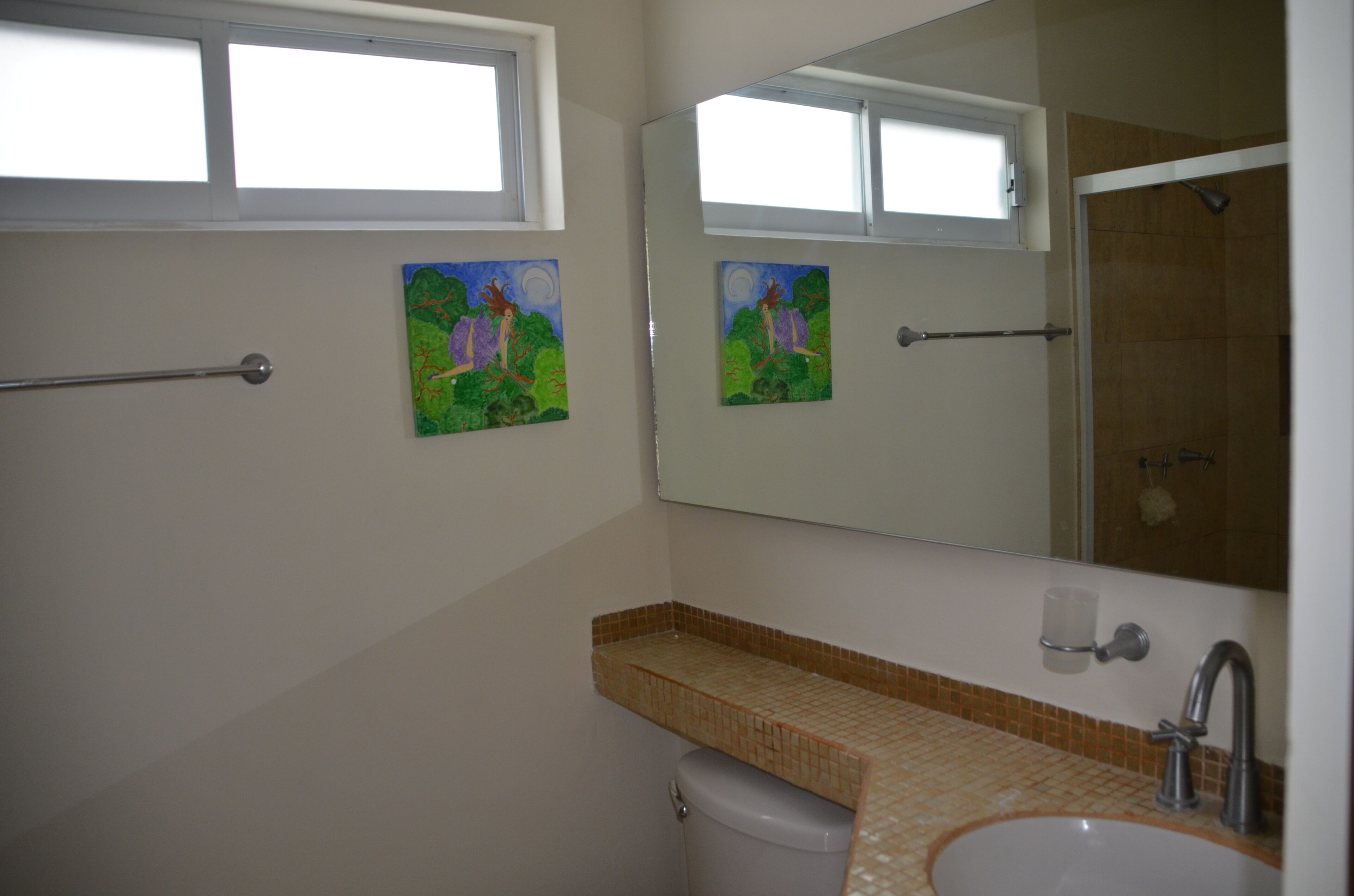 Ein Badezimmer mit Fenster, Toilette, Waschbecken und zwei Bildern an der Wand.
