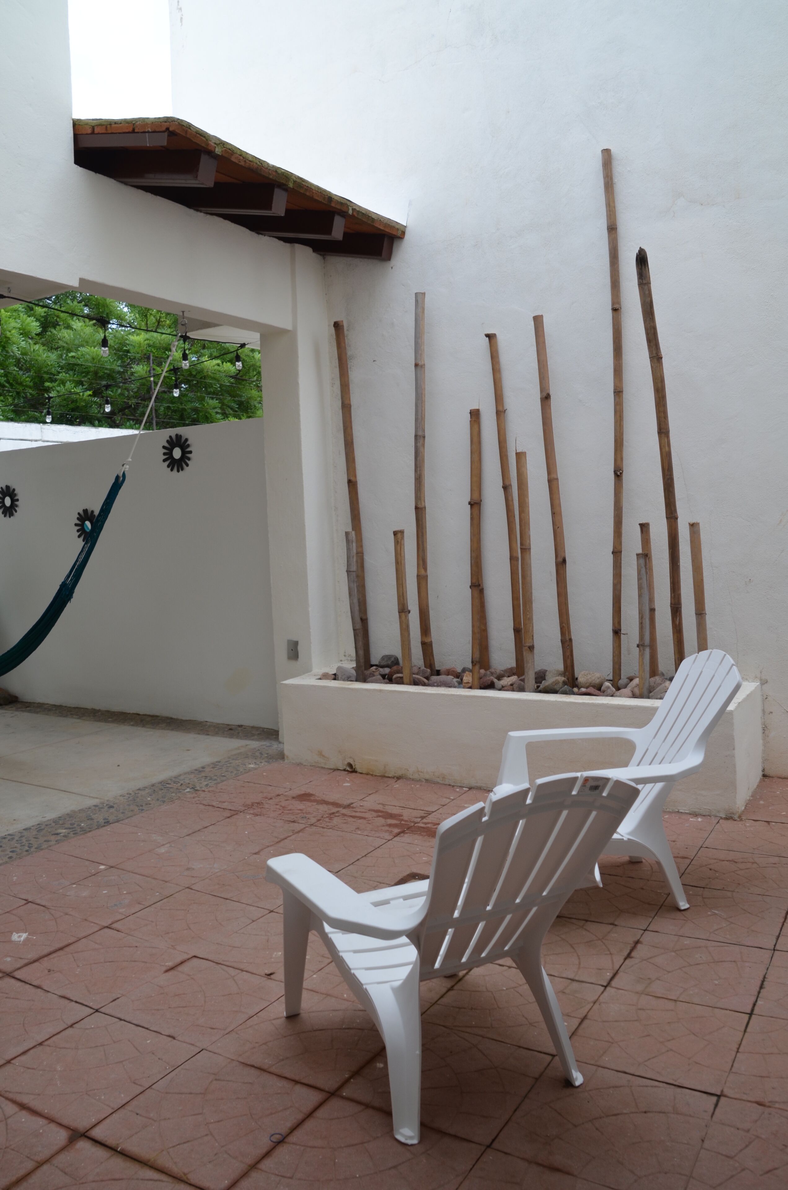 A patio with two white chairs, a hammock, and a bamboo wall.