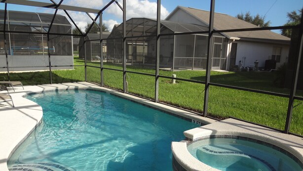A swimming pool with a hot tub, surrounded by a covered area with a view of houses.