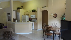 A living room with a sofa, a dining area with chairs and a table, a kitchen with appliances, and a TV.