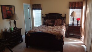 A bedroom with a large bed, a dresser, a nightstand, a lamp, a painting, and a window with blinds.