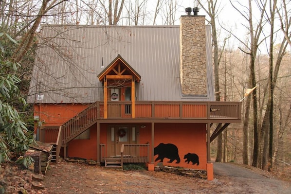 A cabin with a stone chimney, a porch with a bear mural, and a wooden staircase.