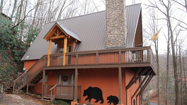 A cabin with a stone chimney, wooden balcony, and a bear mural.