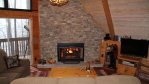 A cozy living room with a stone fireplace, wooden beams, a television, and a sofa.