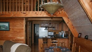 A cozy cabin interior with a dining area, kitchen, and a staircase leading to a loft.