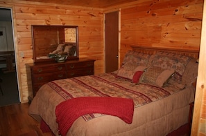 A wooden-paneled bedroom with a bed, dresser, and mirror.