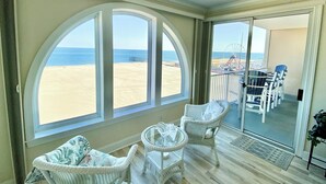 A room with large arched windows overlooking a beach, wicker furniture, and a balcony with a view of the ocean and a pier. - 🏖️Fabulous Ocean Front Unit Belmont Towers 802 🏖️ (Ocean City)