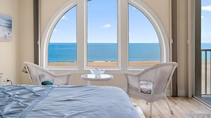 A bedroom with a large bed, two wicker chairs, a small table, and a view of the ocean through arched windows. - 🏖️Fabulous Ocean Front Unit Belmont Towers 802 🏖️ (Ocean City)