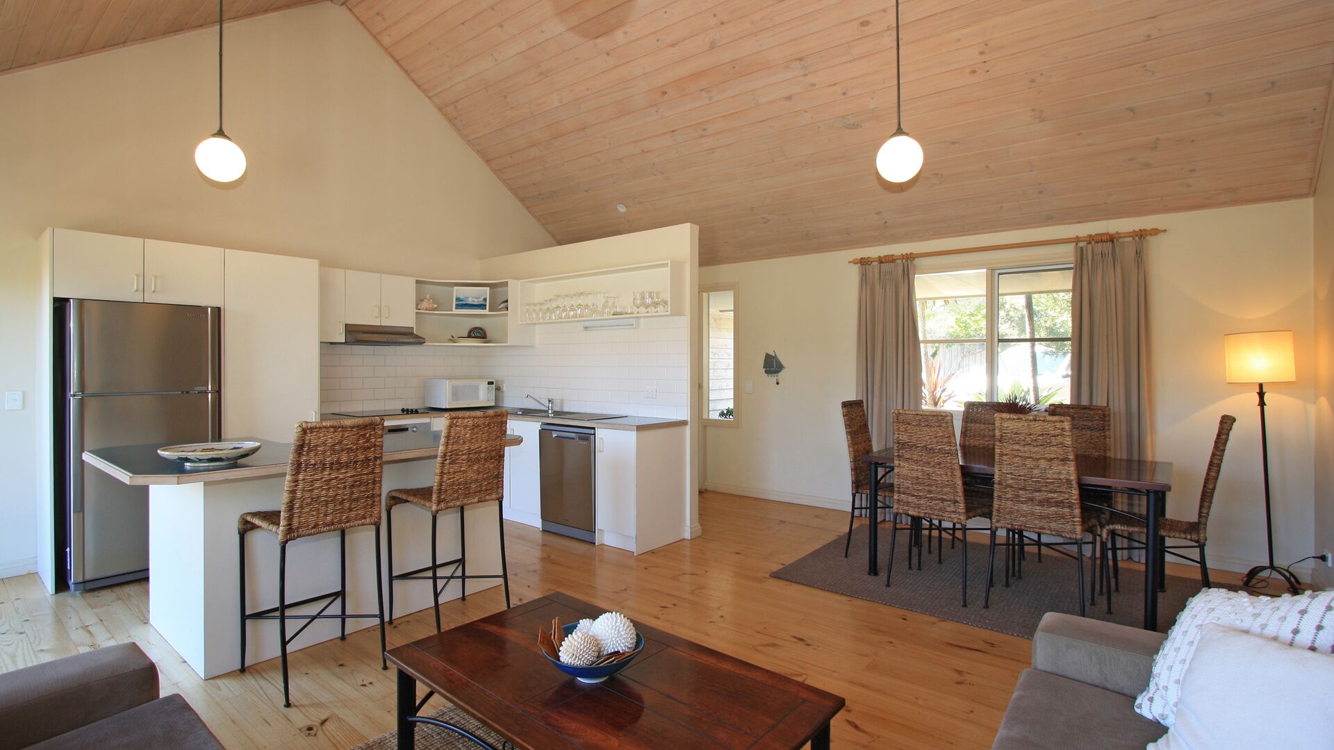 A modern kitchen with white cabinets, a stainless steel refrigerator, and a dining area with wicker chairs and a table.