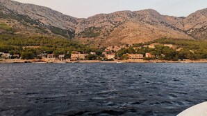 A coastal town with buildings along the shoreline, a rocky mountain backdrop, and a body of water in the foreground. - Apartments Arboreum A2 (5+2) (Ivan Dolac)