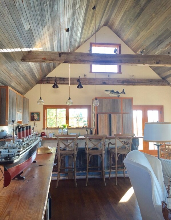 A rustic kitchen with wooden beams, a large ship model, and a dining area with wooden chairs.