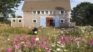 A two-story house with a blue door and windows, surrounded by a garden with various flowers. - Hope House on Rhode Island's South Shore sits on 6 private acres (Little Compton)