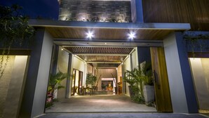 A modern building entrance with a covered walkway, potted plants, and a well-lit interior. - Ocean View Villa Bali (Ungasan)