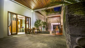 A spacious indoor courtyard with stone flooring, a wooden ceiling, and a large stone column. There are potted plants and a seating area with tables and chairs. - Ocean View Villa Bali (Ungasan)