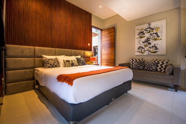 A modern bedroom with a large bed, a sofa, wooden paneling, and a wall-mounted artwork. - Ocean View Villa Bali (Ungasan)