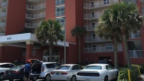 Un hotel de varios pisos con fachada roja, balcones y un estacionamiento con coches.