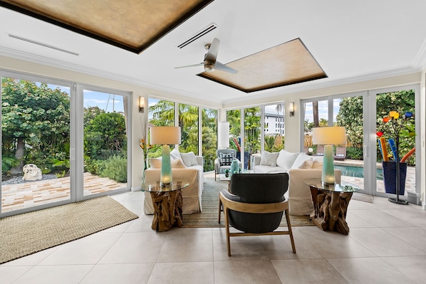 Una habitación amplia con un gran ventanal, ventilador de techo y una zona de estar con mesa y sillas.
