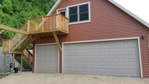 Ein rotes, zweistöckiges Haus mit einer Holzterrasse und zwei Garagen.