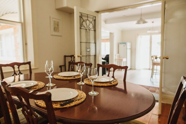 A dining table set with plates, cutlery, and wine glasses, surrounded by wooden chairs.