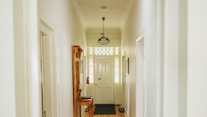 A narrow hallway with wooden flooring, a black rug, and a door at the end leading to a room with a chandelier. - Cooke Cottage- Right on the Riesling Trail (Clare)