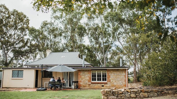 A stone house with a metal roof, a patio with chairs and a table, and a large umbrella. - Cooke Cottage- Right on the Riesling Trail (Clare)