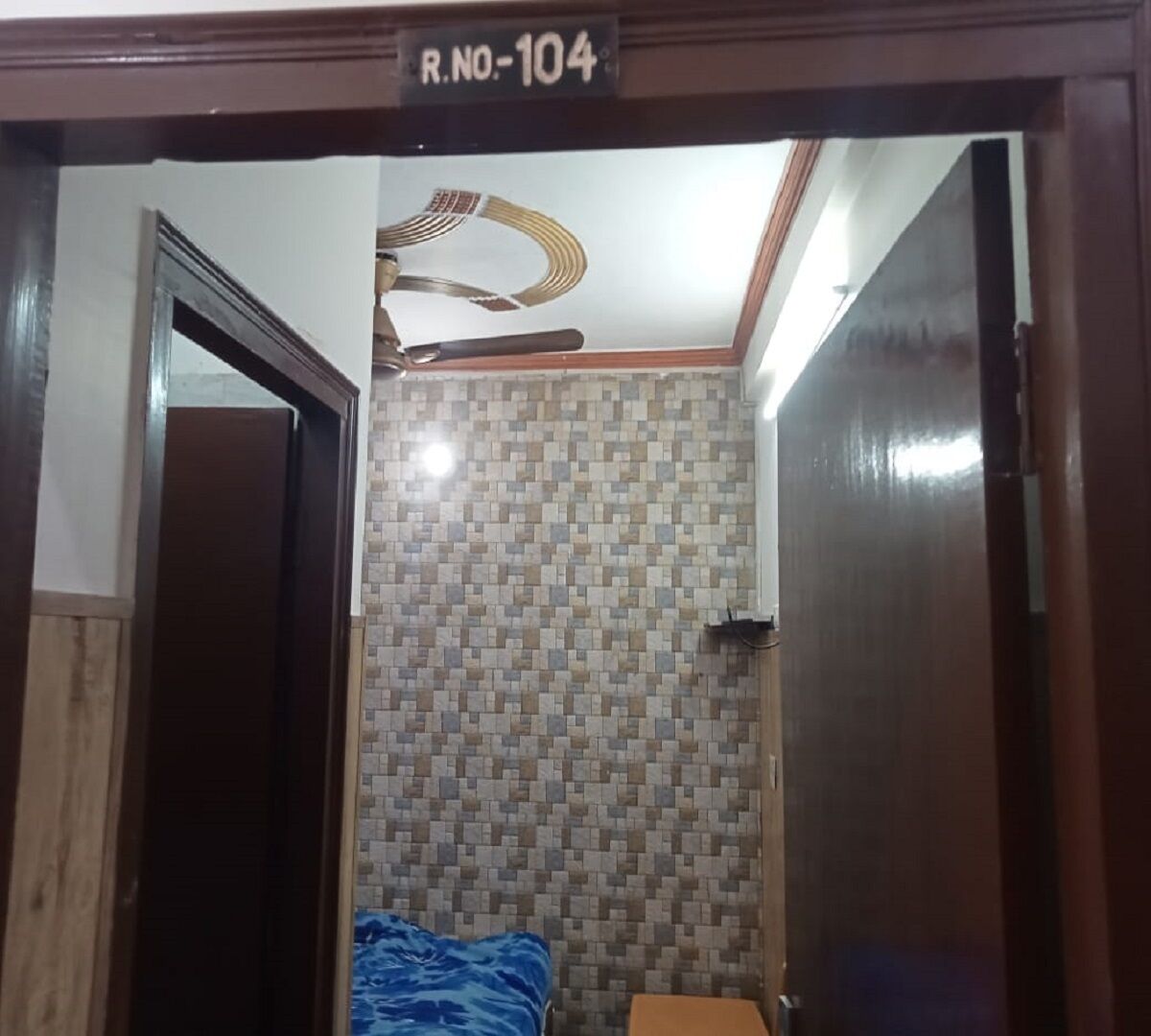 A room with a tiled wall, a bed with a blue cover, and a wooden door with a sign above it.
