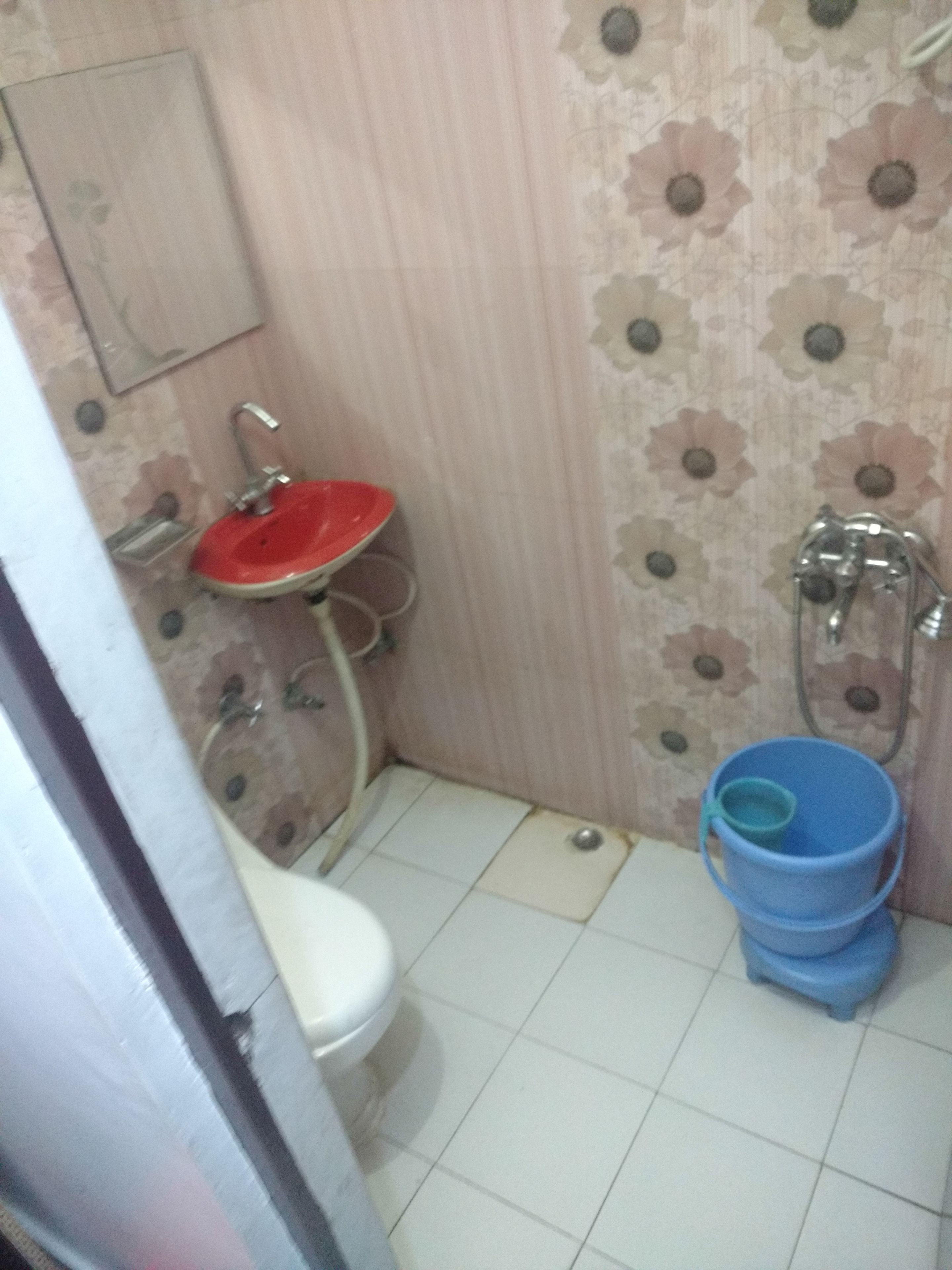 A bathroom with a red sink, white toilet, and blue bucket.